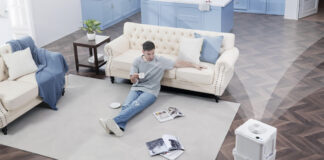 An overhead view of a man sitting on a living room floor with a Midea Cube dehumidifier in the bottom, right corner.