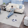 An overhead view of a man sitting on a living room floor with a Midea Cube dehumidifier in the bottom, right corner.