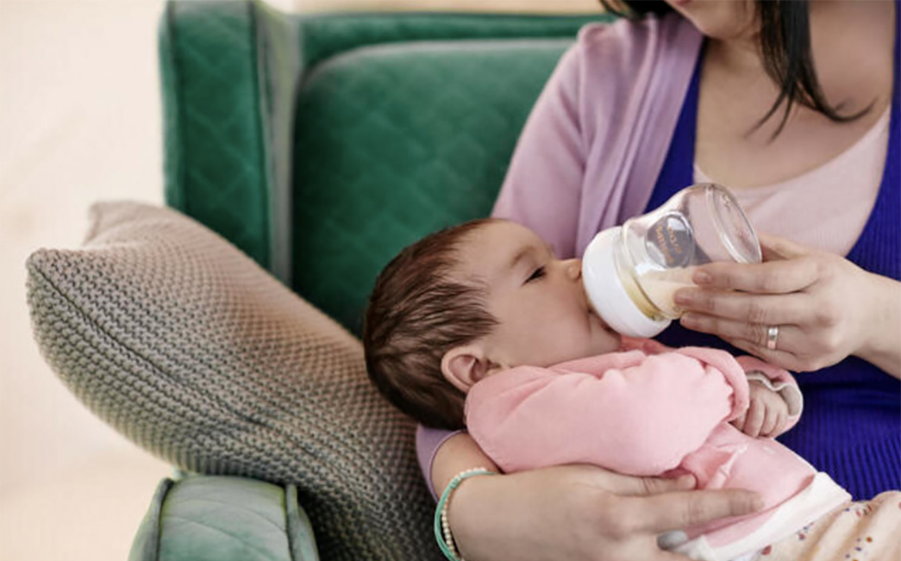 A woman feeding a baby using a Philips Avent BPA-free bottle.