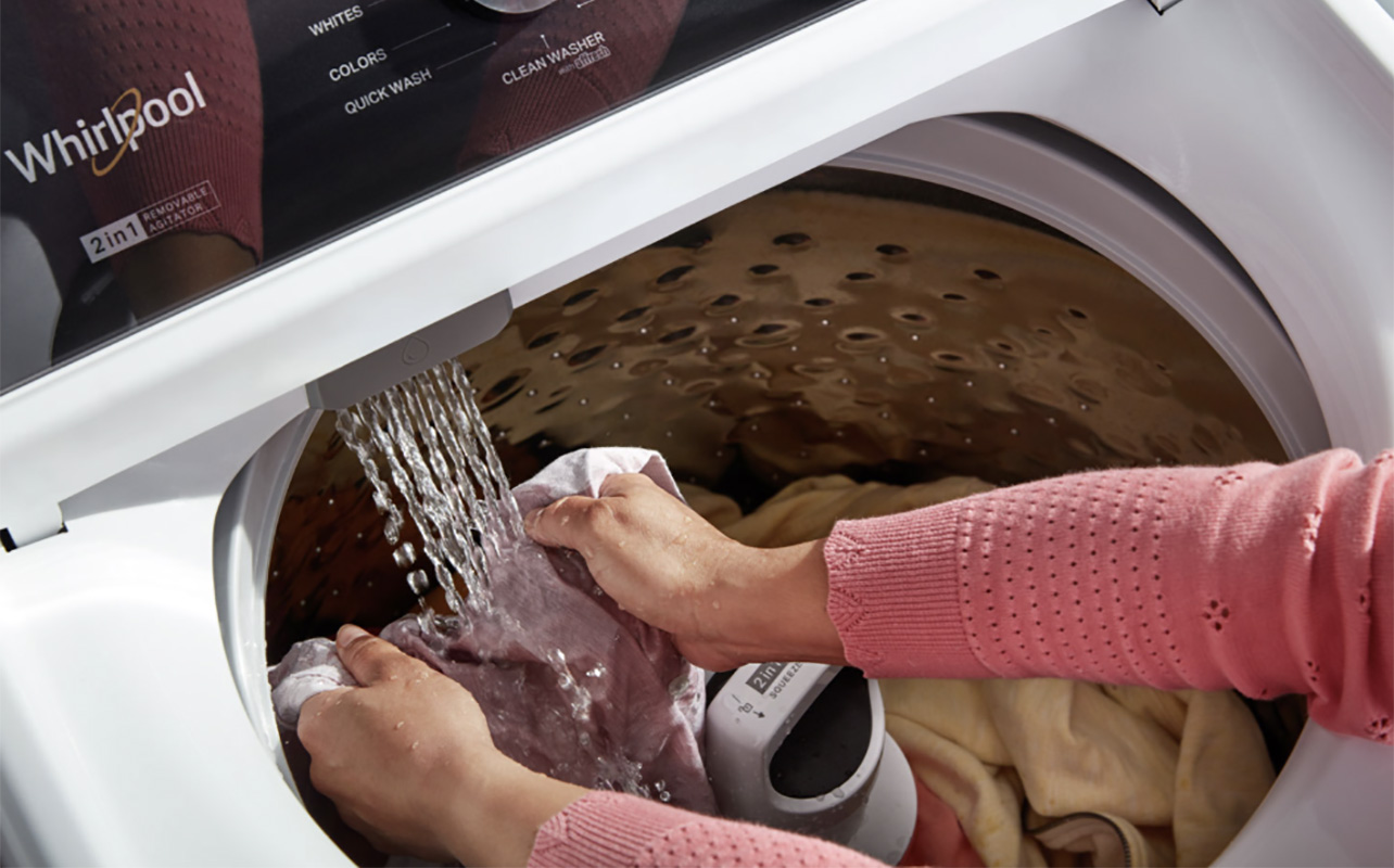 A close-up of clothing in a Whirlpool top load washer with hands rinsing something.