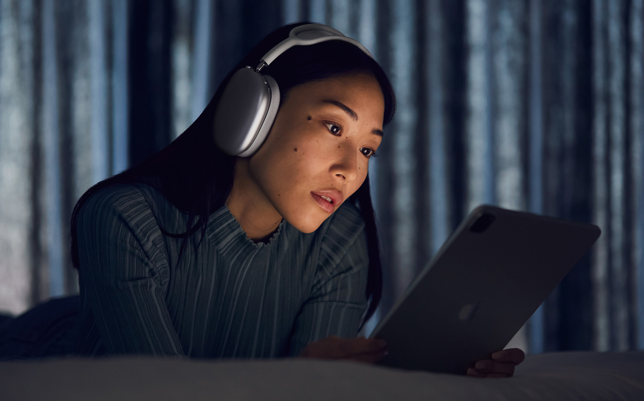 Woman wearing Apple AirPods Max in silver in darker room.