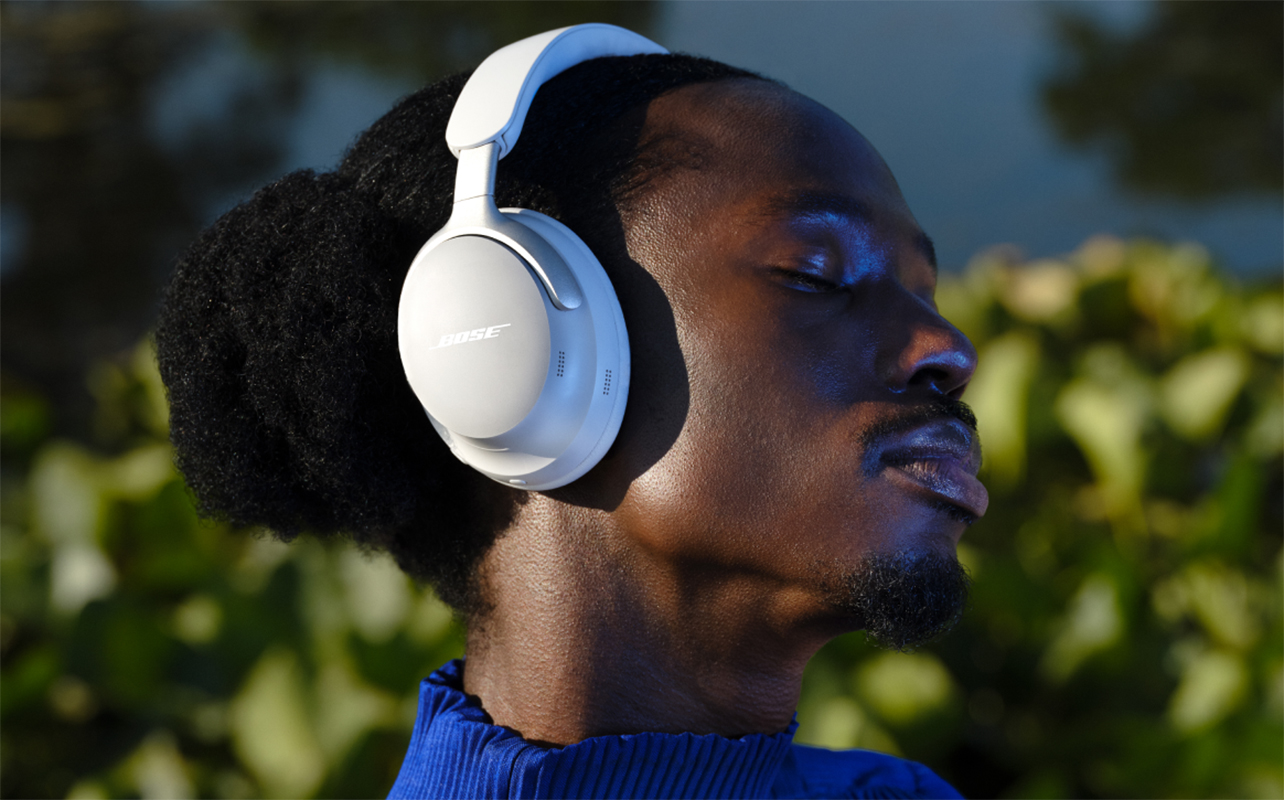 Man wearing white Bose QuietComfort Ultra headphones outside.