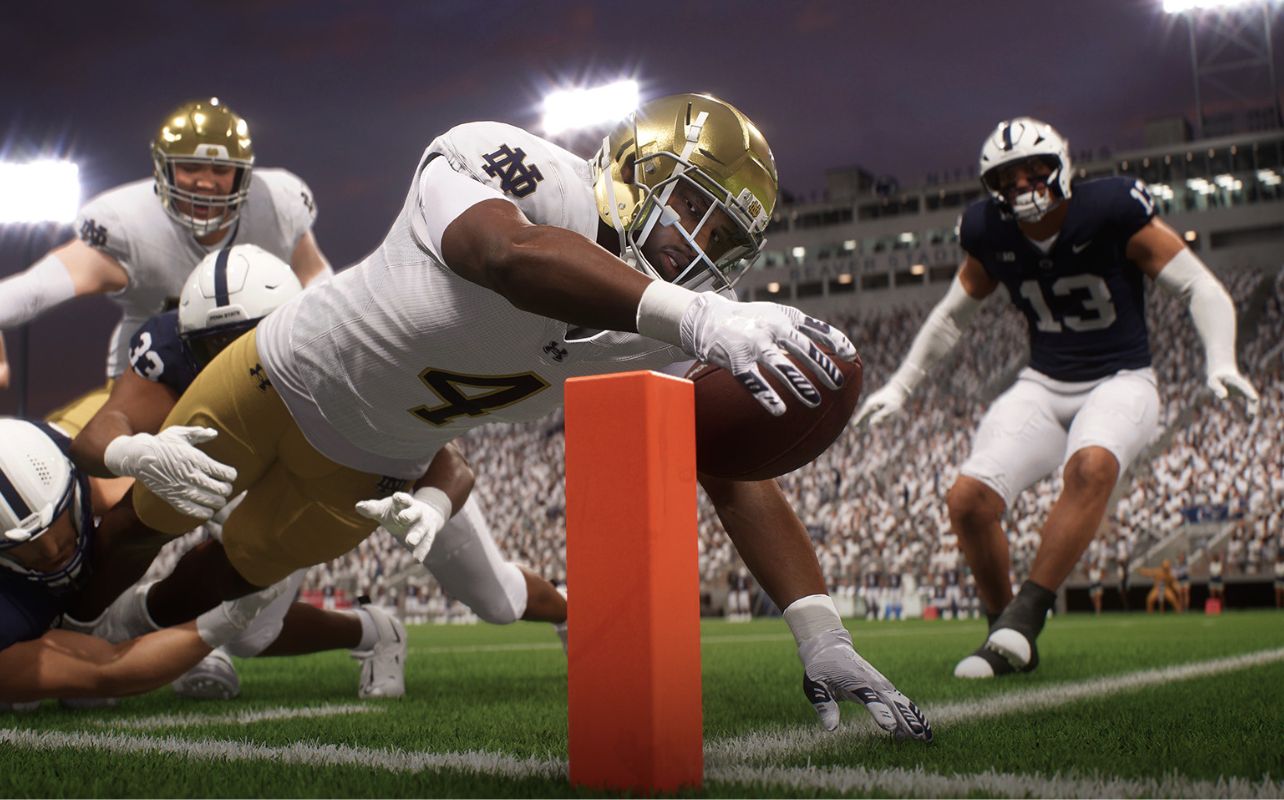 Football player in gold helmet dives with ball over goal line pylon, surrounded by opposing players in navy. Stadium lights shine brightly.