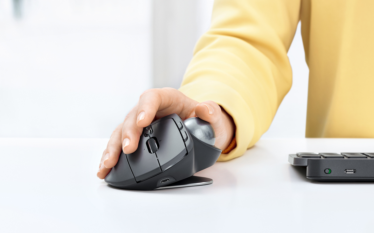Person using Logitech MX Ergo mouse and trackball on desk.