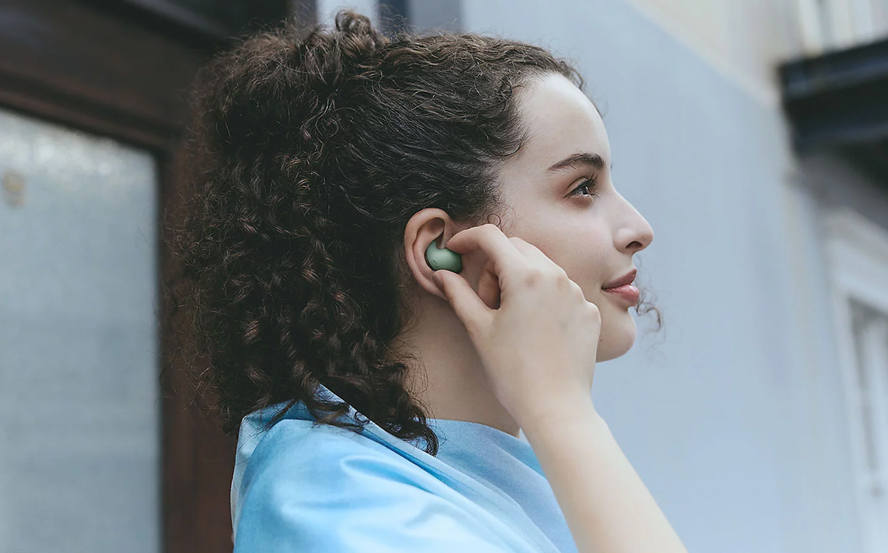 Woman putting Sony LinkBuds Fit in green into left ear.