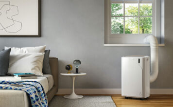 A De'Longhi portable air conditioner being vented out of a window in a bedroom.