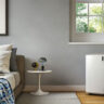 A De'Longhi portable air conditioner being vented out of a window in a bedroom.
