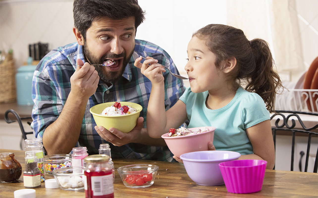 Father and daughter putting sprinkles on ice cream