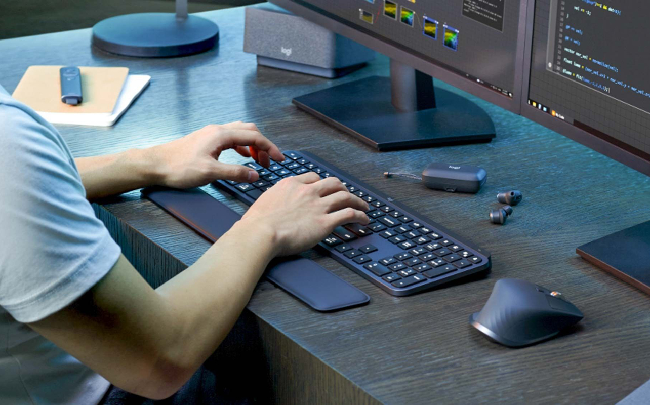 Man working at desk with Logitech MX keyboard and mouse system.