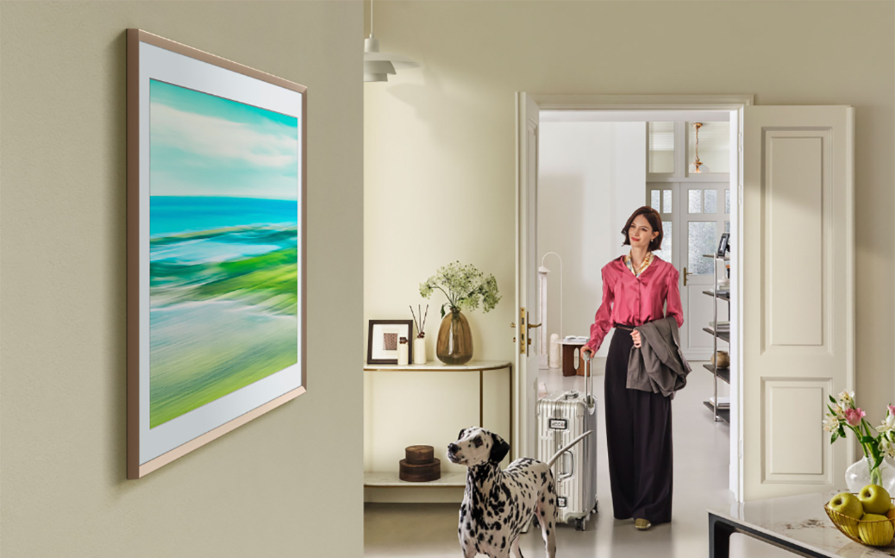 a woman standing in th hallway, a Samsung The Frame TV mounted on the wall on the side.
