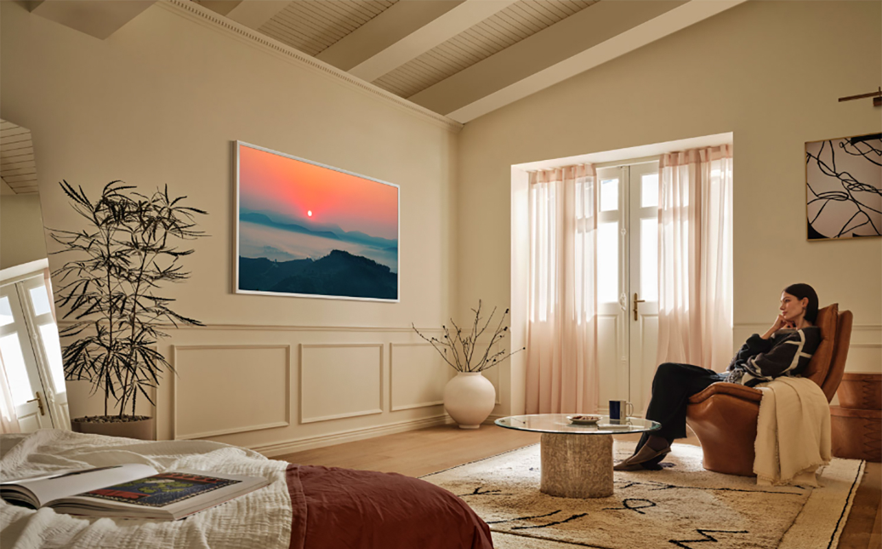 A woman sitting on a chair watching a Samsung The Frame Pro TV, which is mounted on the wall.