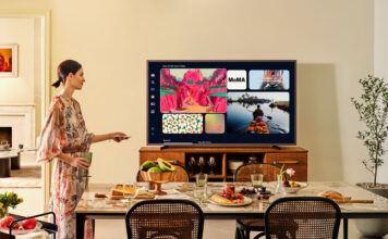 A woman standing beside the Samsung The Frame Pro TV mounted on furniture.