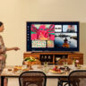 A woman standing beside the Samsung The Frame Pro TV mounted on furniture.