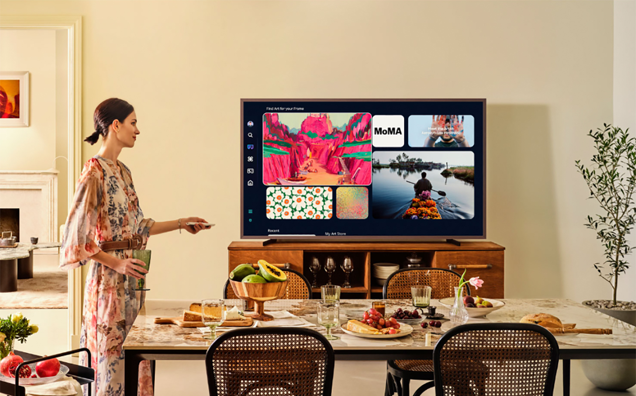 A woman standing beside the Samsung The Frame Pro TV mounted on furniture.