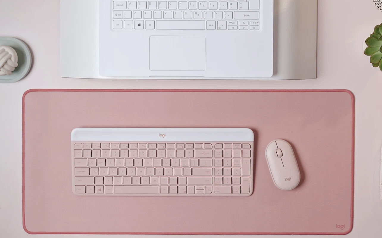 Logitech MK470 Slim Combo in pink on similar background in front of laptop.