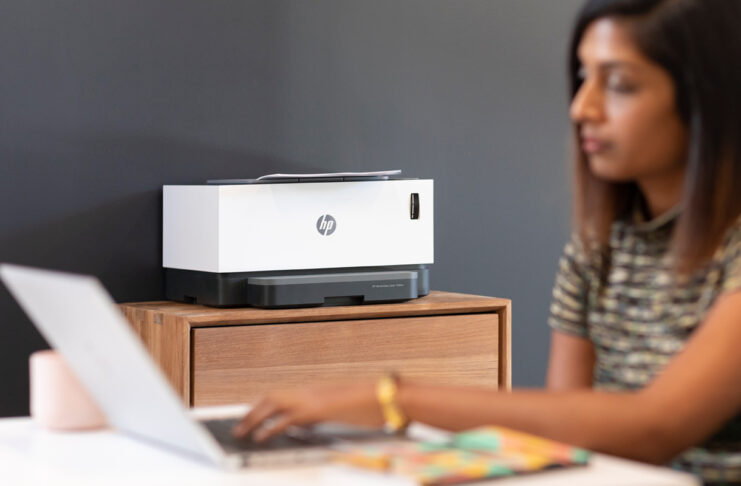 Woman on laptop with HP wireless printer in background.