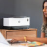 Woman on laptop with HP wireless printer in background.
