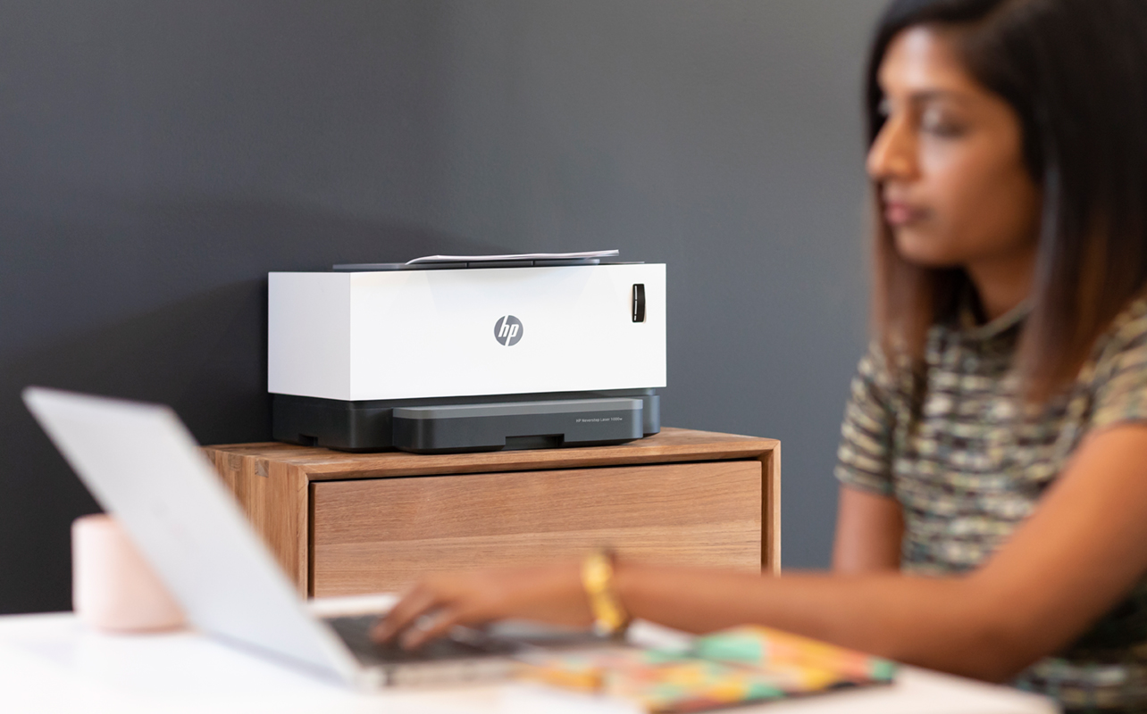 Woman on laptop with HP wireless printer in background.