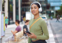 Young female student wearing white JBL headphones on campus.