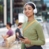 Young female student wearing white JBL headphones on campus.