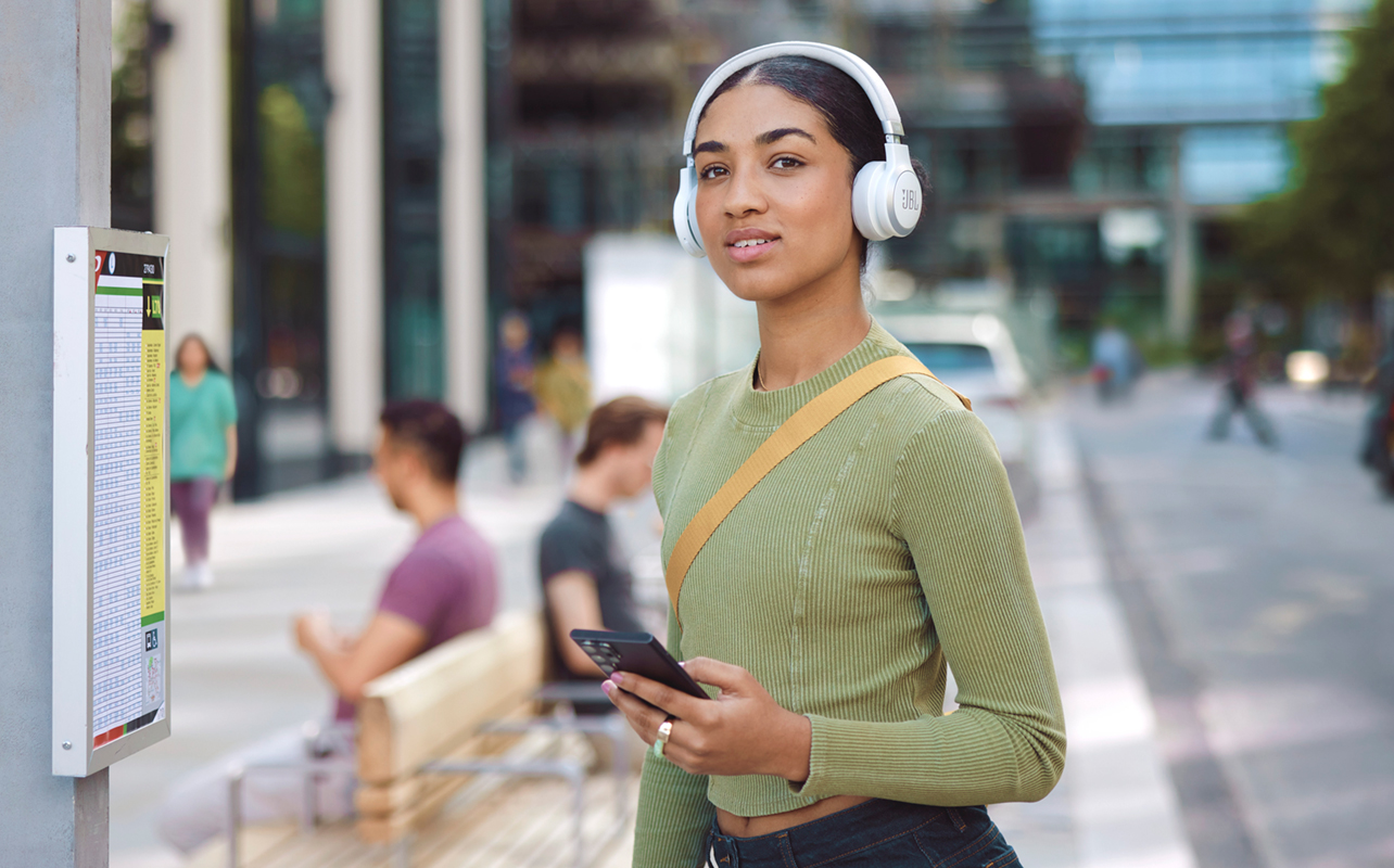 Young female student wearing white JBL headphones on campus.