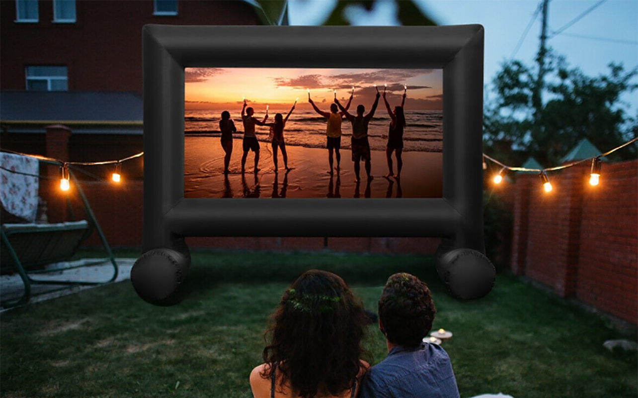 A couple on a blanket outside watching a movie on a portable projector screen.