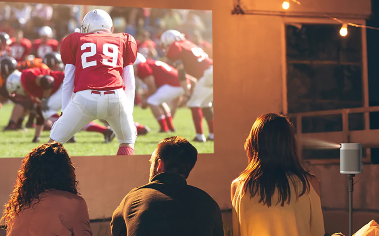 Two people watching football outside using a projector and screen.