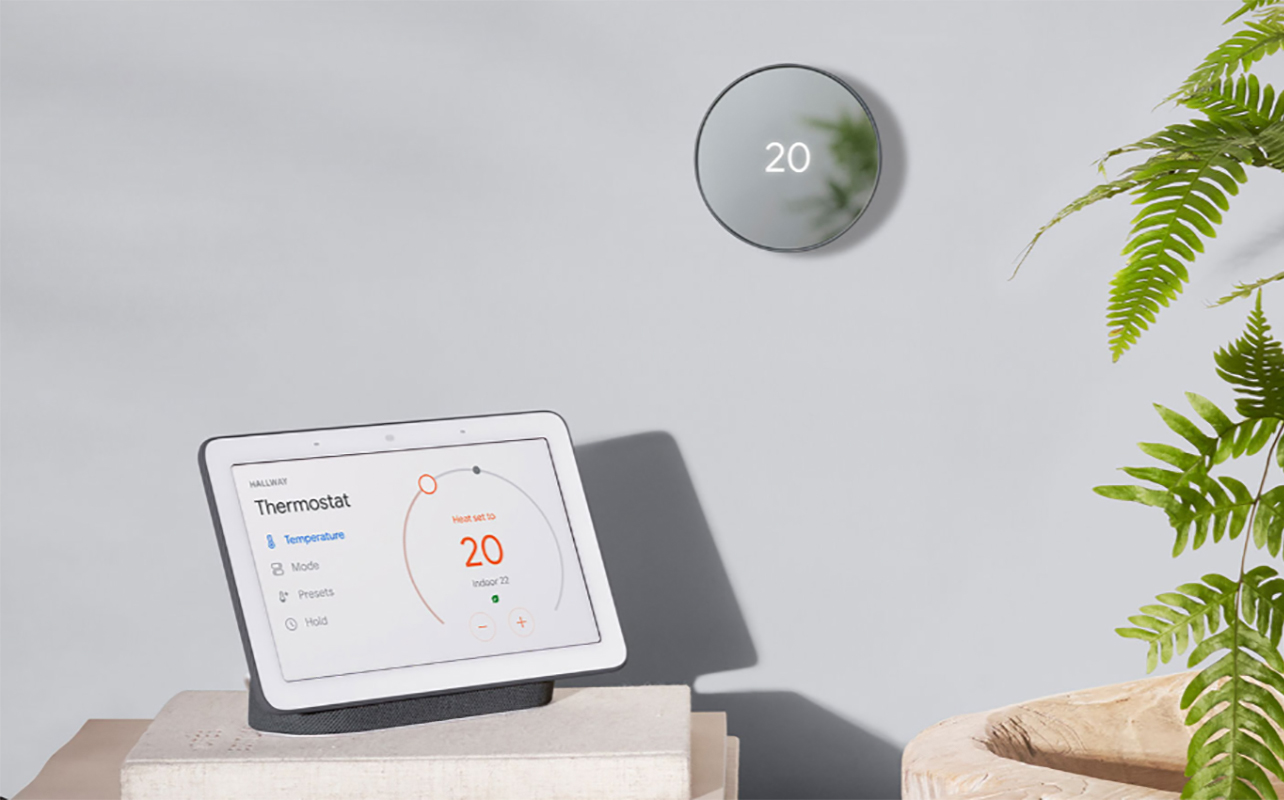 A Google Nest Wi-Fi smar thermostat mounted on the wall beside a Google Nets smart display showing its reading.