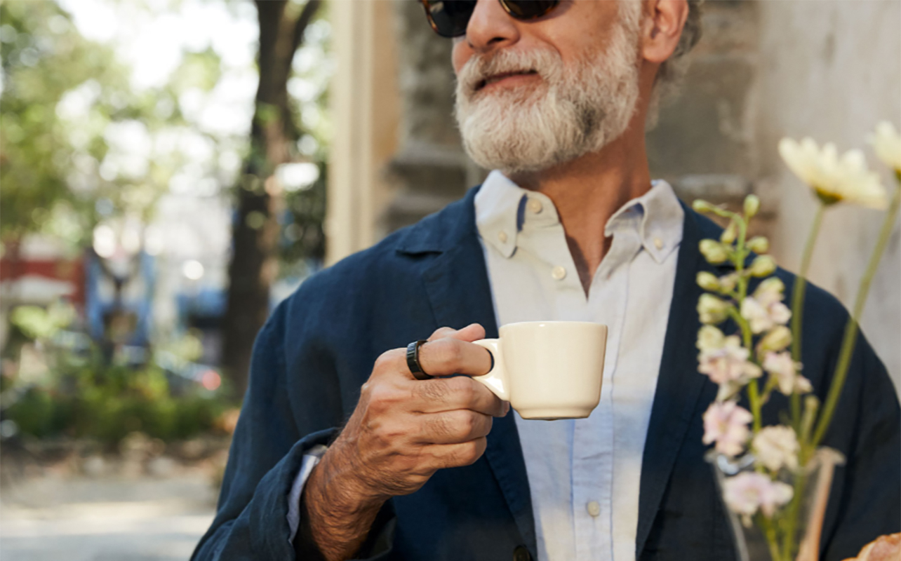An elderly man sitting on a patio with coffee wearing the Oura Ring 3.