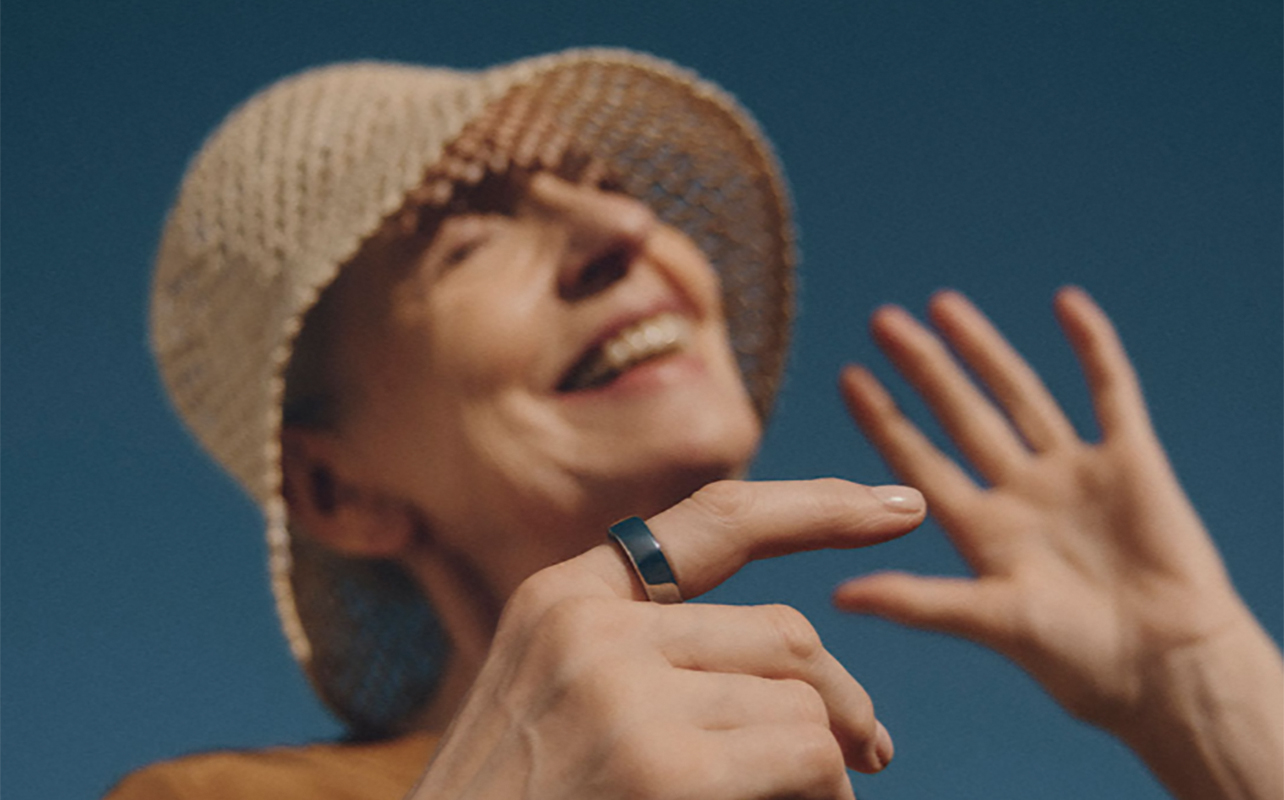A woman in a hat smiling while wearing the Oura Ring 3.