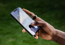 A man's hand holding a phone and wearing the Ultrahuman Ring Air.