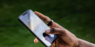 A man's hand holding a phone and wearing the Ultrahuman Ring Air.