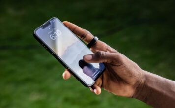 A man's hand holding a phone and wearing the Ultrahuman Ring Air.