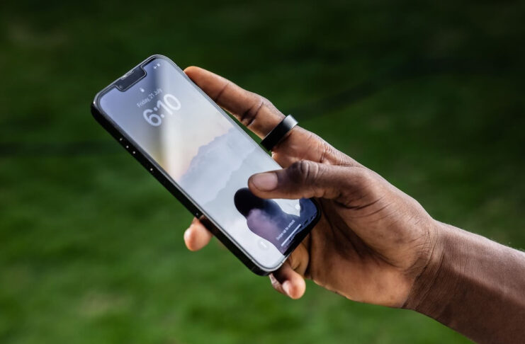 A man's hand holding a phone and wearing the Ultrahuman Ring Air.