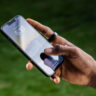 A man's hand holding a phone and wearing the Ultrahuman Ring Air.
