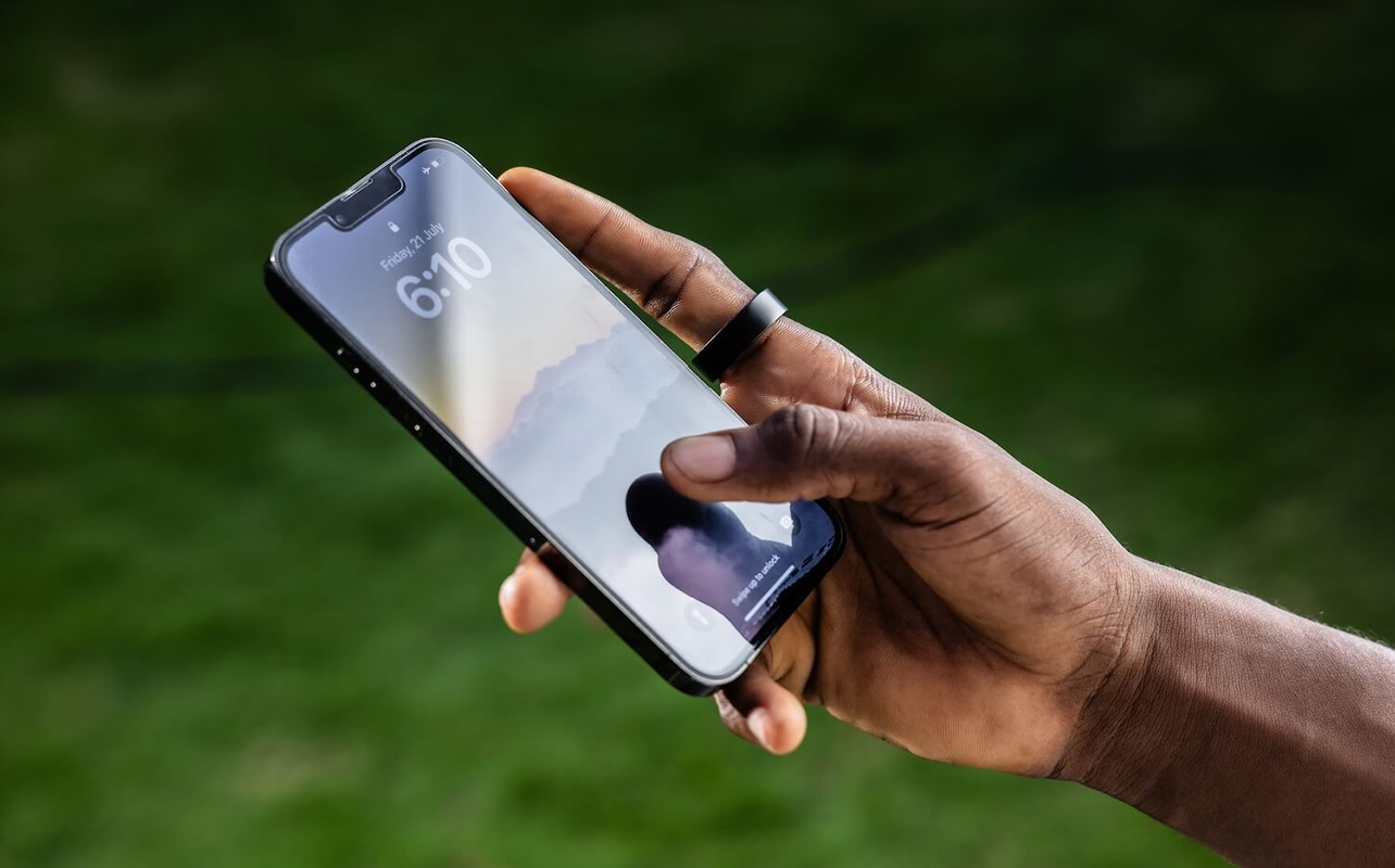 A man's hand holding a phone and wearing the Ultrahuman Ring Air.
