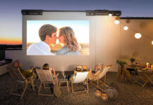 Four people sitting outside on folding chairs in front of a screen using an Xgimi portable projector.