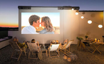Four people sitting outside on folding chairs in front of a screen using an Xgimi portable projector.