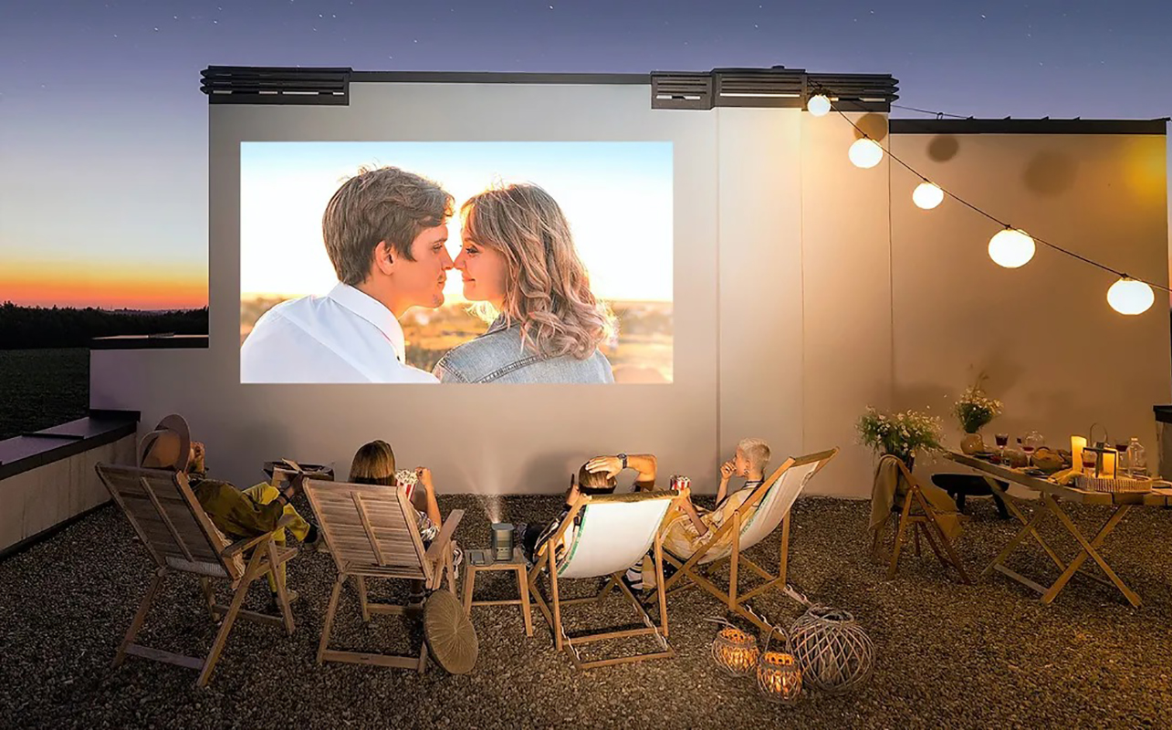 Four people sitting outside on folding chairs in front of a screen using an Xgimi portable projector.