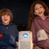 Two kids in a tent outside with a Yaber T2 projector between them.