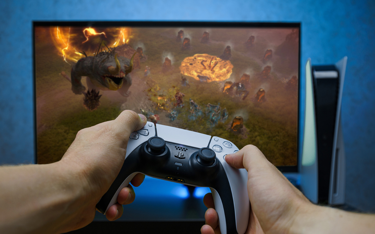 Close-up of hands holding controller playing a console game on a monitor.