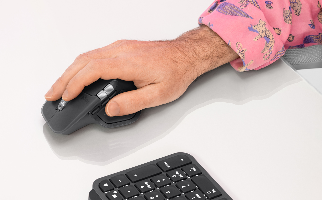 Man holding Logitech MX Master 4 mouse in black next to a keyboard.