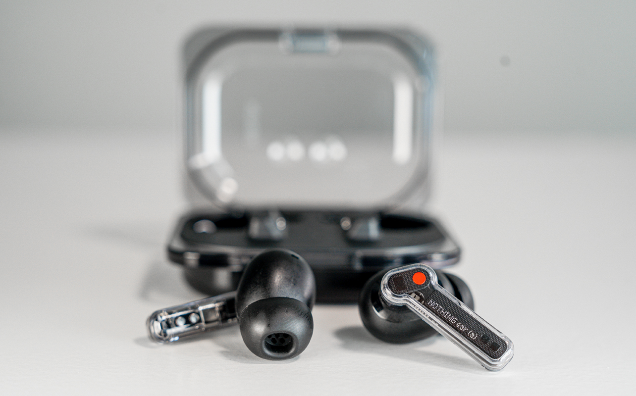 Nothing Ear (a) wireless earbuds loose in front of case.