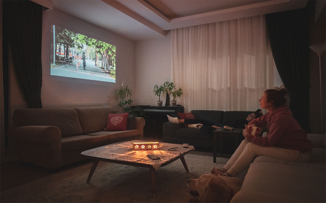 Woman watching home cinema projection - gifts for film lovers - with her dog in the living room at home.