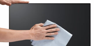 Man's hands wiping dry a computer monitor with a microfibre cloth.