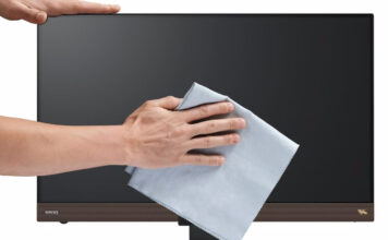 Man's hands wiping dry a computer monitor with a microfibre cloth.