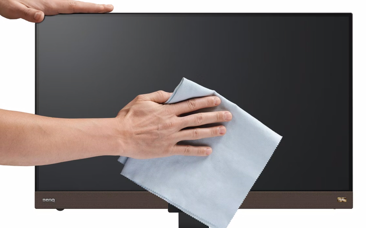 Man's hands wiping dry a computer monitor with a microfibre cloth.
