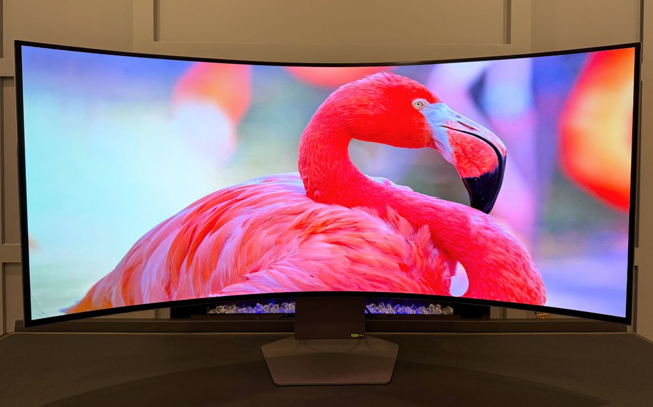 A vibrant flamingo is displayed on a large curved LG UltraGear 5K2K screen with a blurred, colourful background, showcasing vivid pink and red hues.