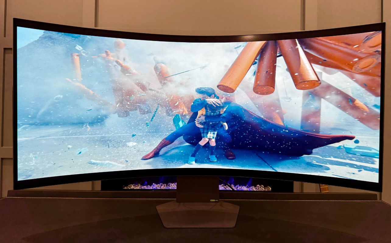 The LG UltraGear 5K2K's curved screen displays a superhero protecting a child amid flying debris and destruction, with vivid colours and a dynamic, intense scene.