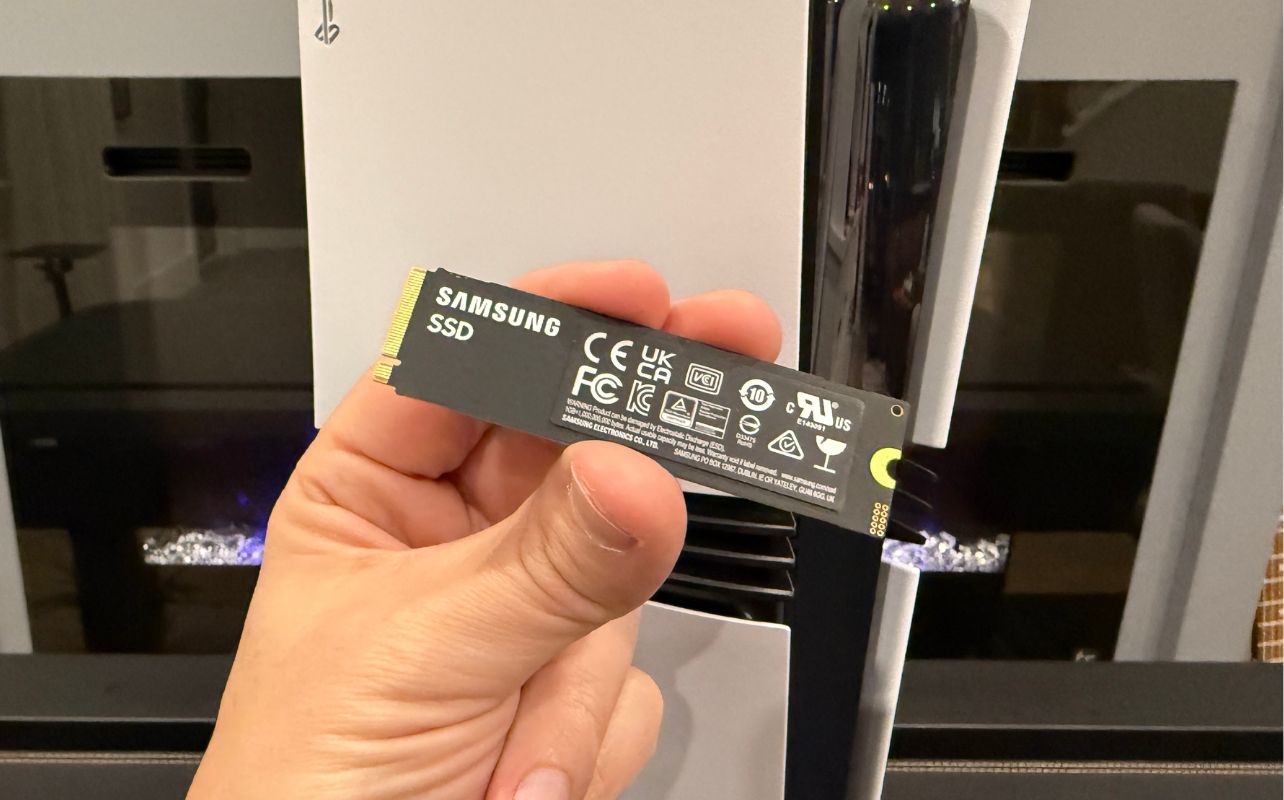 The back of the Samsung 9100 Pro SSD in front of the PS5 Pro gaming console which is sitting straight up.